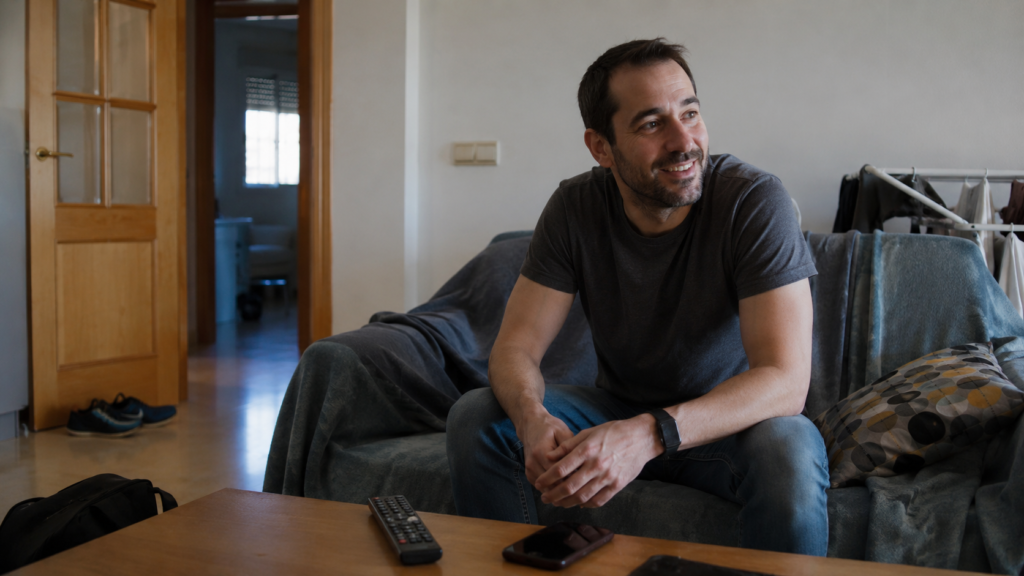 Hombre sentado en un salón cotidiano mostrando una mezcla de alivio y anticipación